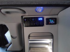 Campervan electrical control panel with power sockets, illuminated voltage display and digital heater controller.