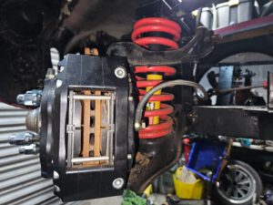 Close-up of a vehicle brake assembly and suspension with a red coil spring and yellow shock absorber.
